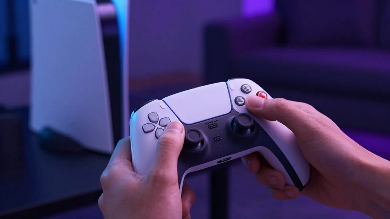 Manos de una persona sujetando un mando inalámbrico frente a una consola en una habitación con luces LED.